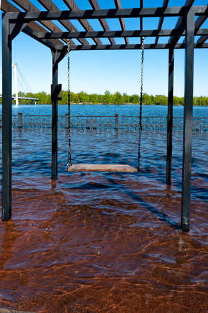 Hanging swing for children on the flooded embankment. Hanging swing on chains with a wooden seat.の写真素材
