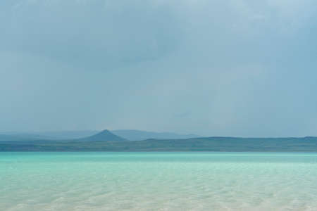 The opposite shore of the azure lake against the background of the rainy sky. The sky is covered with dark clouds above the horizon. Texture for the background.の写真素材