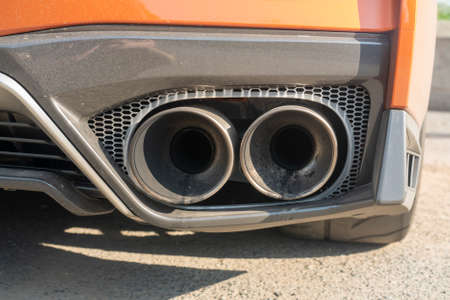 Twin tailpipes of an orange sports car. Details of a sports car on a bright sunny day.