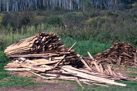Lumber stockpiled in the open air on the green grass. Procurement of fuel for winter heating of the...