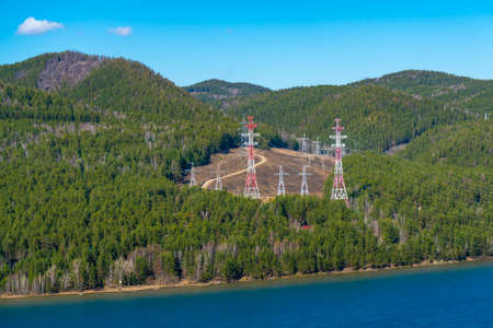Red-white Electric poles at the edge of the forest. Power lines across the river.の写真素材