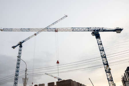 Metal cranes against the background of the cloudy sky. Construction of residential buildings.