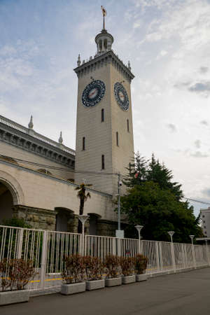 A high column of a building with a city clock against a cloudy sky. The building is fenced in front of the sidewalk.の写真素材