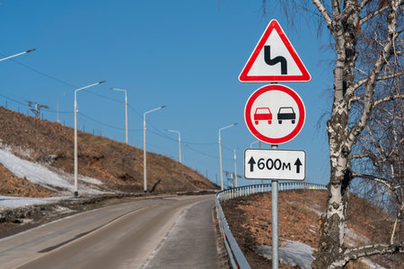 Road signs on a pole at the side of the road. Winding road sign prohibition of overtaking 600 meters.の写真素材