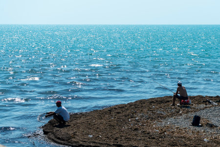 Fishermen sit on the seashore with fishing rods. Fishing from the seashore.の写真素材
