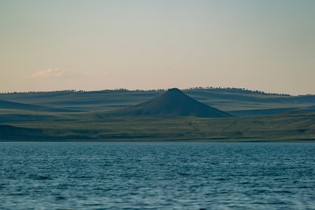 A mountain in the middle of a plain on the shore of a lake. The lake shore against the evening sky.の写真素材