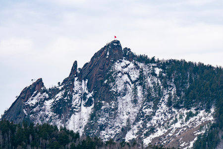A rock with a red flag on the mountaintop. The rock is set against a cloudy winter sky.の写真素材