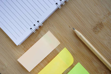 note book, pencil, sticky paper memo arrows on the wooden table background