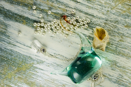 Pendant on a chain and seashell and glass swan figure among scattered pearls on old white board.の写真素材