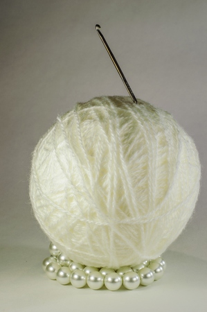 White ball of yarn and hook for knitting and pearl beads on a light background.の写真素材