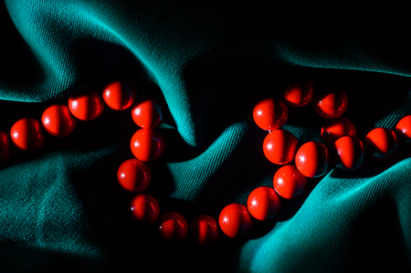 Red coral beads in tough dramatic shadows on a dark green background along the frame.の写真素材