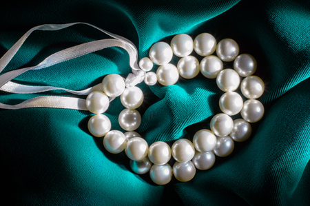 White pearl bracelet with a white ribbons on dark green velvet.の写真素材