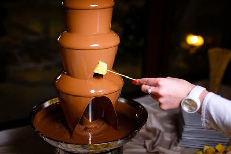 female hand with skewer takes piece of apple into chocolate  fondueの写真素材