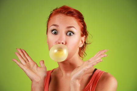 funny redhead girl with bubble gum on green backgroundの写真素材