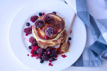 Pancakes with berries and honey on white tableの写真素材
