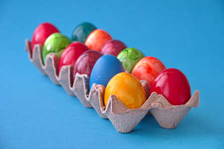 Colorful Easter eggs in cardboard box against blue backgroundの写真素材