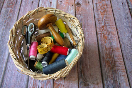 Different sewing items in wicker basket on wooden background