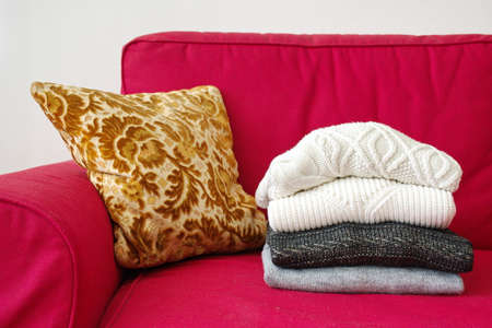 Closeup shot of warm sweaters and cushion on red sofa in living roomの写真素材