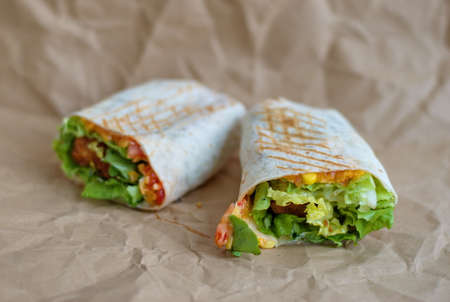 Closeup of tortilla with fried chicken meat and vegetables on sheet of paperの写真素材