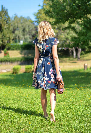 Beautiful blond woman in the park holding her shoes in handの写真素材