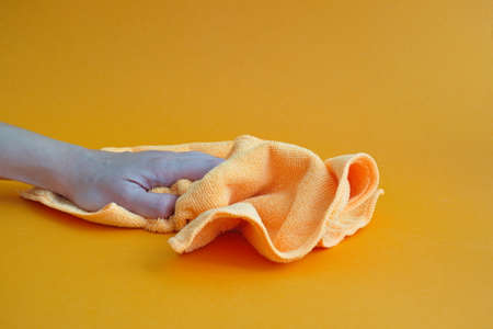 Woman's hand holding orange microfiber cloth against orange backgroundの写真素材