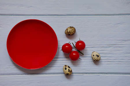 Red plate, cherry tomato and quail eggs on wooden backgroundの写真素材