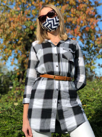 Mature woman in black and white plaid shirt and black and white face mask in autumn nature