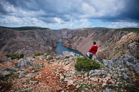 Rear view of woman sitting on the rock above river canyonの写真素材