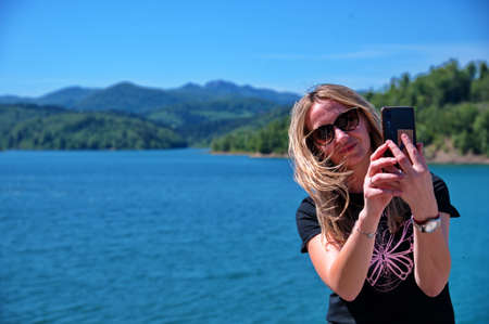 Mature woman sitting at the lake shore and using mobile phone