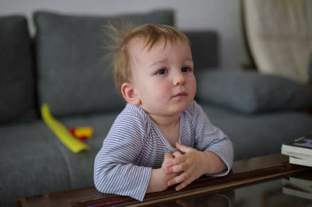 Portrait of cute little boy standing in living room beside sofa