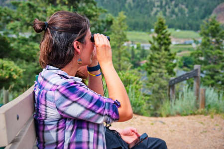 Mature woman sitting on the bench and using binocularsの写真素材