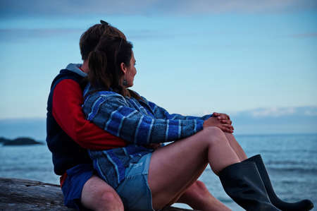 Mature couple sitting on a tree trunk on the beachの写真素材