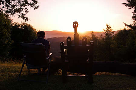 Rear view of woman sitting in the nature during sunset with acoustic guitar beside her