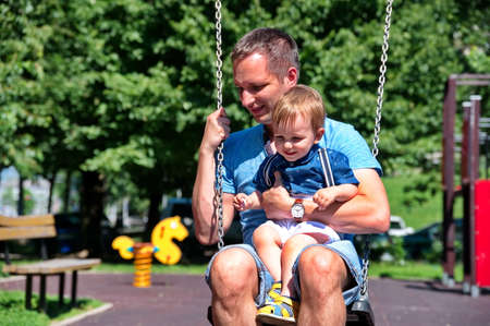 Father swinging with his little boy on playgroundの写真素材