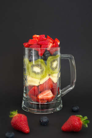 Berry fruit, apple and kiwi cut and put in the glass against the black backgroundの写真素材