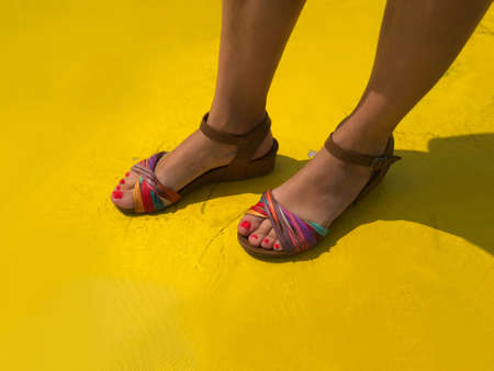 high angle view of woman's feet with colorful sandals on yellow backgroundの写真素材