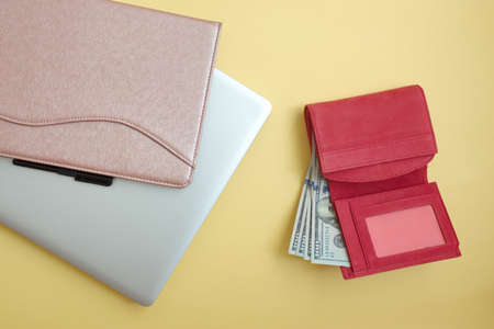 Red wallet with dollar banknotes, tablet and laptop against the yellow backgroundの写真素材