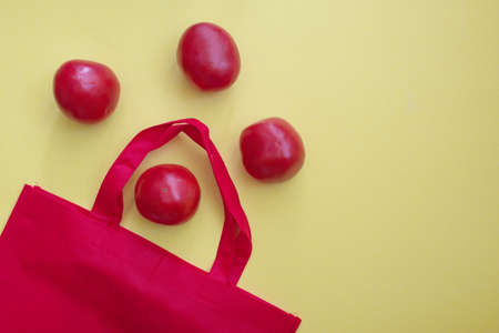Red reusable shopping bag with tomatoes against the yellow backgroundの写真素材