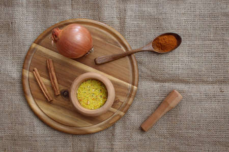 Spices in wooden bowl and wooden spoon, onion and cinnamon on the wooden cutting board. Directly above shotの写真素材