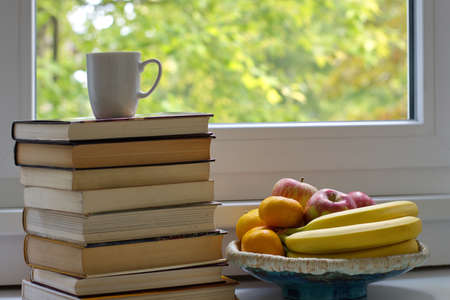 Books and bowl with fruits on the table against the windowの写真素材