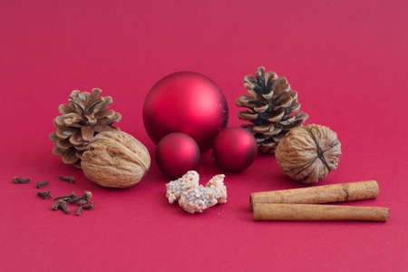 Christmas balls, pinecone, nuts and cinnamon against the red backgroundの写真素材