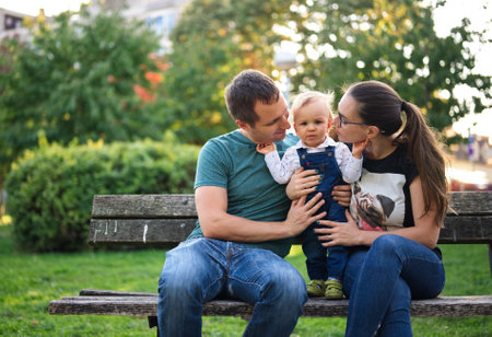 Couple sitting on a bench in a park holding their little child
