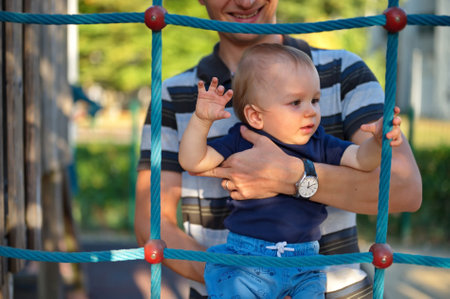 Father holding his little baby boy on playground rope ladderの写真素材