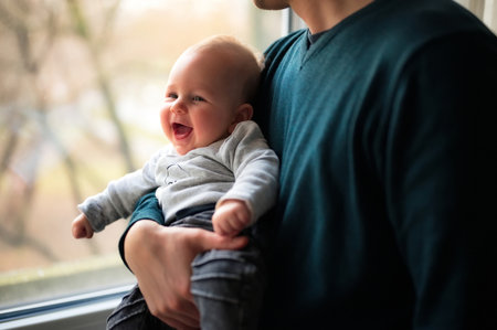 Father standing by the window and holding cute little baby
