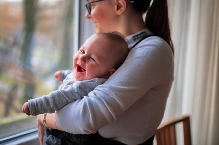 Mother standing by the window and holding cute little babyの写真素材