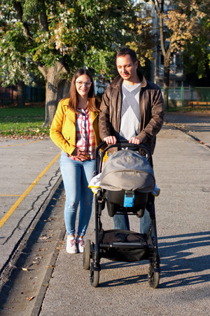 Young couple walking in park and pushing their baby in stroller