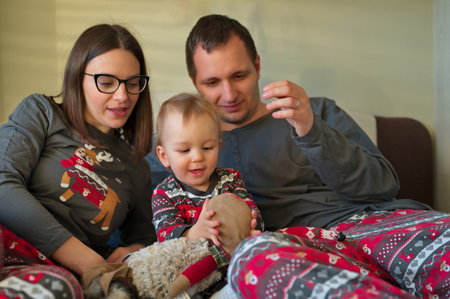Young couple in Christmas pajamas playing with their lovely baby