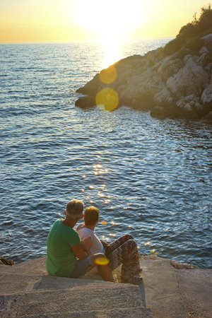 Two mature women sitting on the seashore watching sunsetの写真素材