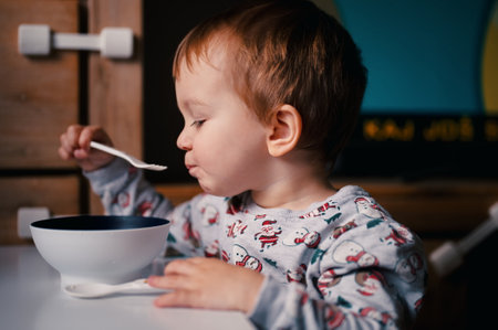 Toddler in Santa shirt sitting and eating with forkの写真素材