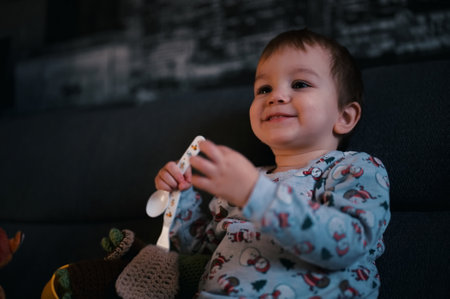 Portrait of cute little toddler sitting on a sofa with his eating utensilの写真素材
